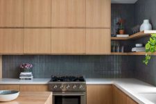 a contemporary blonde wood kitchen with sleek no hardware cabinetry, white stone countertops, a grey skinny tile backsplash