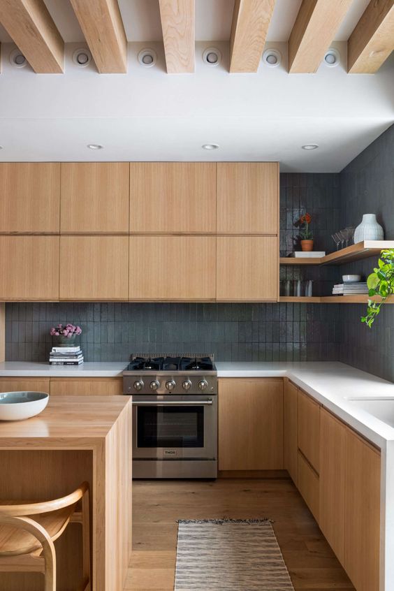 a contemporary blonde wood kitchen with sleek no hardware cabinetry, white stone countertops, a grey skinny tile backsplash