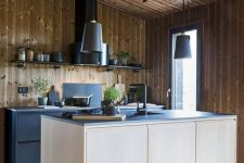 a contemporary chalet kitchen all clad with wood, with black metal cabinets and a plywood kitchen island, black countertops and a black hood
