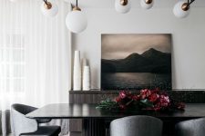 a contemporary dining room with a black statement table, grey curved chairs, a statement artwork, lovely lamps over the table