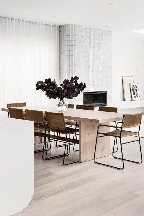 a contemporary dining room with a sleek light stained table, leather chairs, a fireplace clad with white tiles