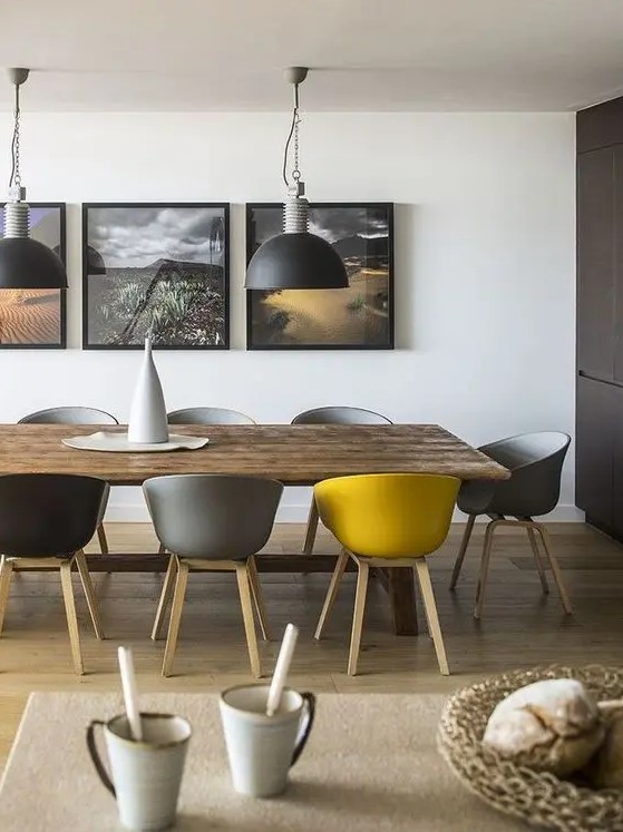 a contemporary grey and yellow dining room, with a wooden table, grey, black and yellow chairs, pendant lamps and a matching gallery wall