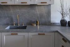 a contemporary grey kitchen with a grey marble backsplash and countertops, brass fixtures is a very chic and bold solution
