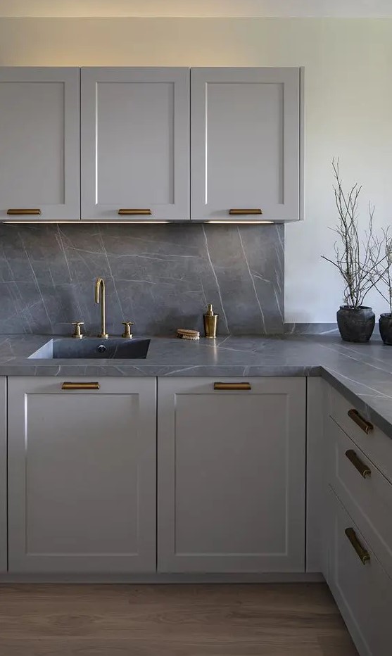 a contemporary grey kitchen with a grey marble backsplash and countertops, brass fixtures is a very chic and bold solution