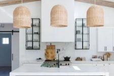 a contemporary kitchen in white, with cabinets with black knobs, a large hood, a black kitchen island with a white countertop and woven pendant lamps