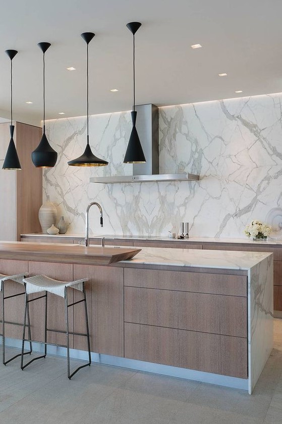 a contemporary kitchen with light-stained cabinets and white marble countertops, a marble backsplash, a large kitchen island with lots of drawers for storage