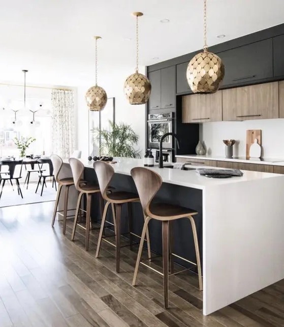 a contemporary kitchen with stained and black cabinets, a black kitchen island, white countertops and a backsplash, gold scale pendant lamps