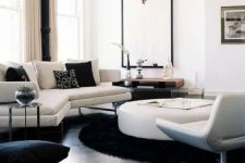 a contemporary living room in black and white, with a black floor, chic white furniture, a round table, a statement artwork and printed pillows