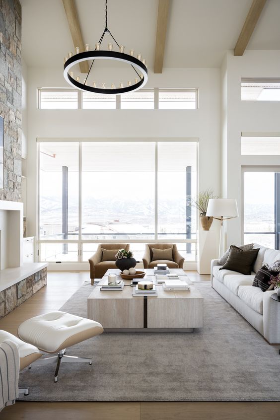 a contemporary living room with a view, a fireplace, a cluster of coffee tables, rust chairs, a neutral sofa and a neutral chair, a round chandelier