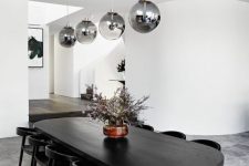 a contemporary monochromatic dining space with a black curved table, black chairs, smoked glass pendant lamps