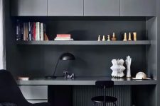 a contemporary moody home office with graphite grey sleek cabinets, an open shelf and a built-in desk, a black chair and a navy one, a black table lamp