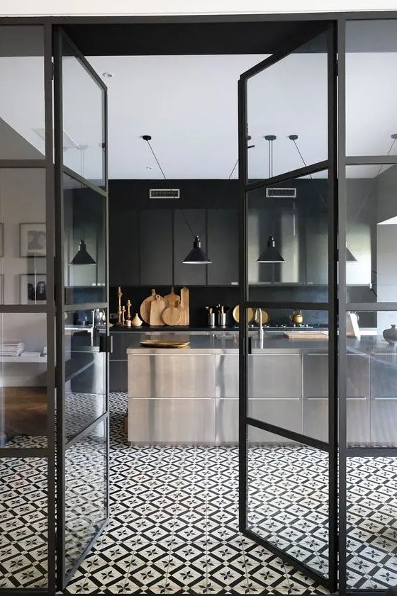 a contemporary moody kitchen with ploished metal cabinets, a black backsplash and countertops plus black pendant lamps
