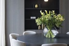 a contemporary sleek dining room with a sleek storage unit, a black statement table, grey chairs and a cluster of pendant lamps