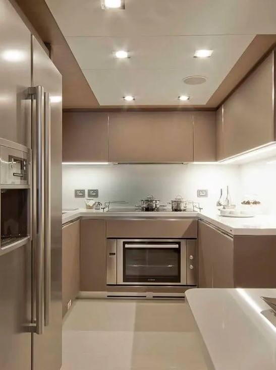 a contemporary taupe kitchen with sleek cabients, white stone countertops and a backsplash, built in lights and neutral appliances
