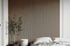 a contemporary to minimalist bedroom with a wooden slat accent wall, a neutral upholstered bed with neutral bedding, a round nightstand and a potted plant