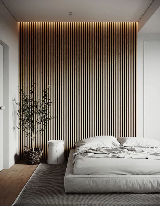a contemporary to minimalist bedroom with a wooden slat accent wall, a neutral upholstered bed with neutral bedding, a round nightstand and a potted plant