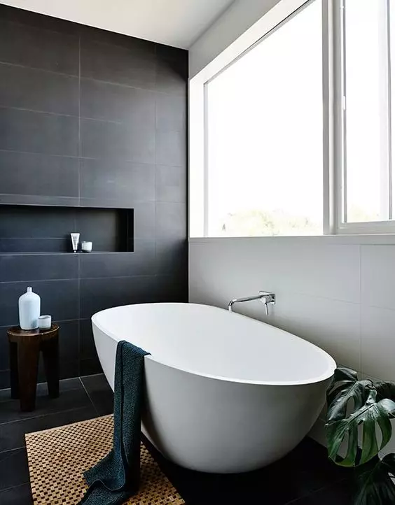 a contrasting contemporary bathroom with black and white tiles, a cool oval tub, a large window and a rug, a potted plant