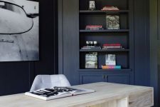 a contrasting home office with navy walls and built-in furniture, a bleached wooden desk and a statement artwork on the wall