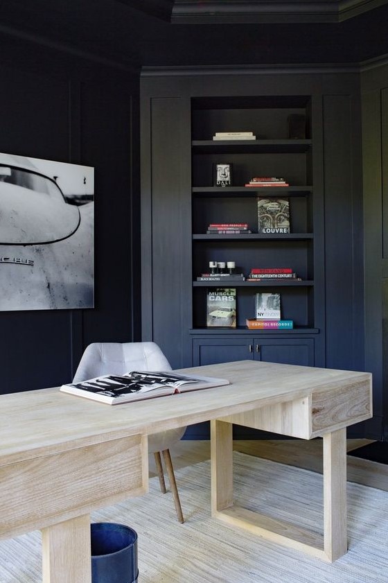 a contrasting home office with navy walls and built in furniture, a bleached wooden desk and a statement artwork on the wall