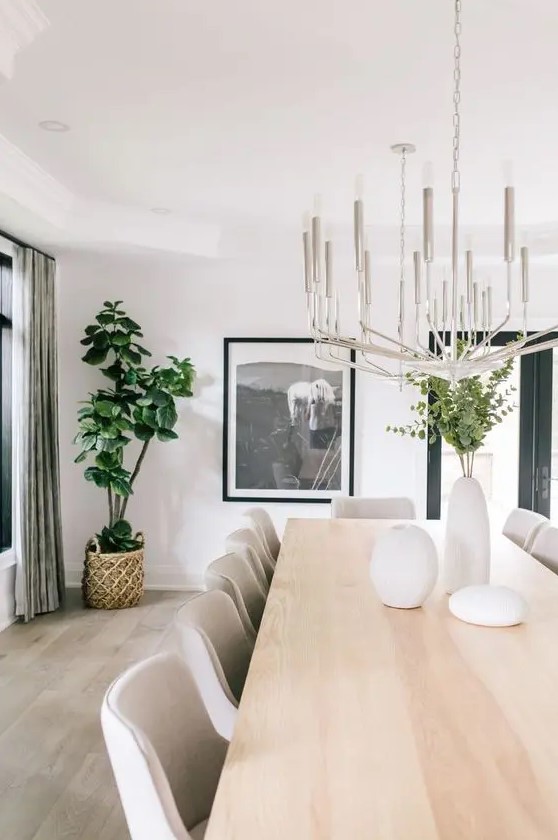 a cool contemporary dining room with a neutral dining table, creamy chairs, a statement chandelier and a bold artwork plus greenery