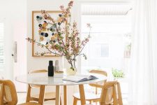 a cool mid-century modern dining spot with a round table, timber chairs, a polka dot artwork and some blooming branches