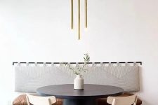 a cool modern dining area with a floating bench with a soft back, a black round table, woven chairs and a lovely gold tube lamp