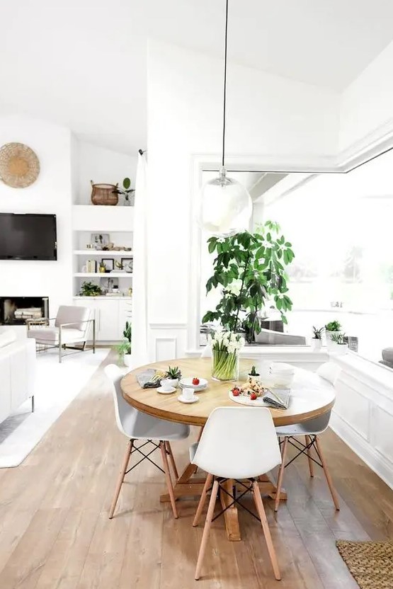 a cool neutral dining space with a corner window, a round table, white chairs, potted greenery and a pendant lamp