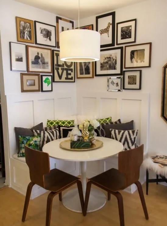 a corner bench with lots of printed pillows, a round table, dark stained chairs, a large gallery wall and a pendant lamp