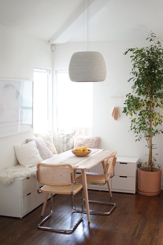 a cozy Scandi dining nook with a corner bench made of IKEA storage units, a table and rattan chairs, a neutral pendant lamp