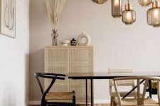 a cozy and warm dining room with greige walls, a black dining table, woven chairs, pendant lamps, a rattan cupboard and some pretty decor