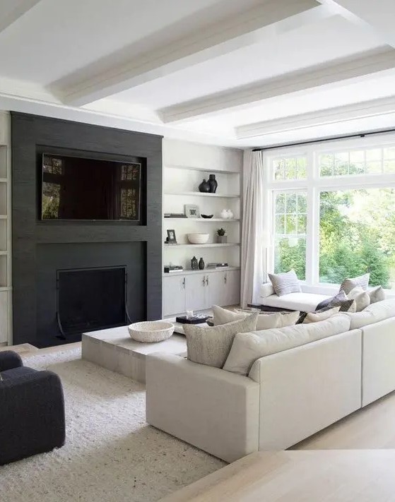 a cozy black and white contemporary living room with a built in TV and fireplace, open shelves, a cabinet, a neutral sofa and daybed, a low table and a black chair