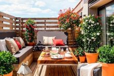 a cozy bright terrace with wooden upholstered benches, a chic coffee tables, potted greenery and flowers