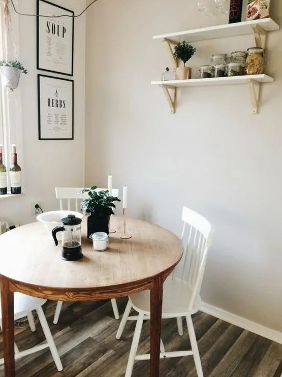 a cozy dining nook with a stained round table, white chairs, open shelves and some greenery in pots has everything necessary