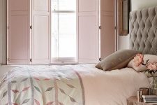 a delicate and welcoming bedroom with grey walls, a grey upholstered bed, blush and grey bedding, pink solid shutters and a catchy pendant lamp