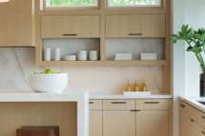 a delicate blonde wood contemporary kitchen with sleke cabinets, white stone countertops and a backsplash, black handles