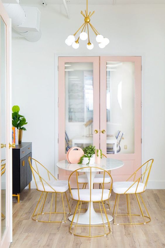 a delicate feminine dining space with a round table and chic gilded chairs, a blush storage unit and a black cabinet
