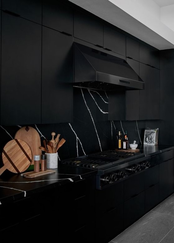a dramatic black kitchen with black marble countertops and a backsplash, with a black hood and appliances is very elegant
