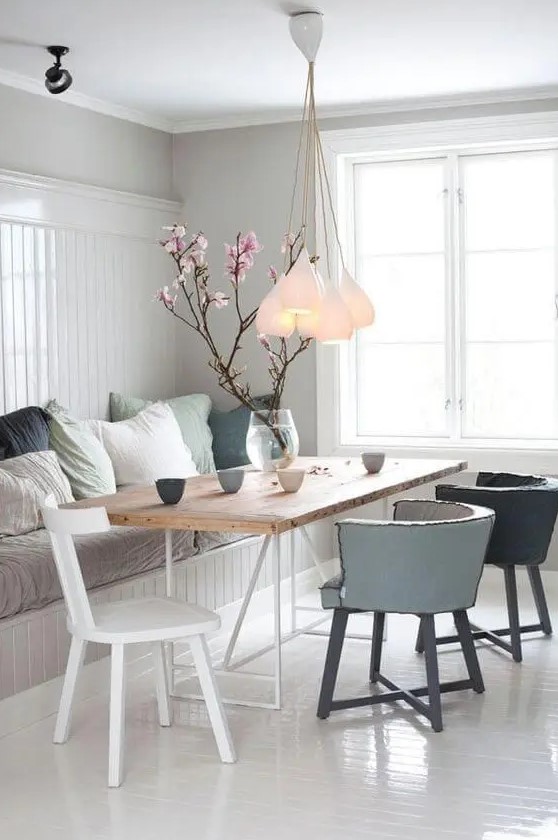 a dreamy Nordic dining space with a built in bench and muted pillows, a wooden table, muted color chairs and a cluster of pendant lamps