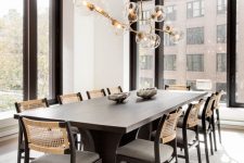 a fab contemporary dining room with a black table, chairs with woven backs, a lovely chandelier with bubbles