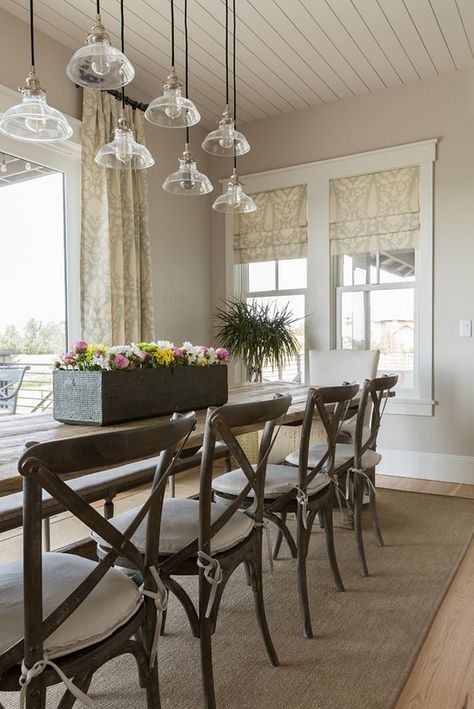 a farmhouse dining room with greige walls, a stained table and chairs and a cluster of clear pendant lamps plus printed curtains