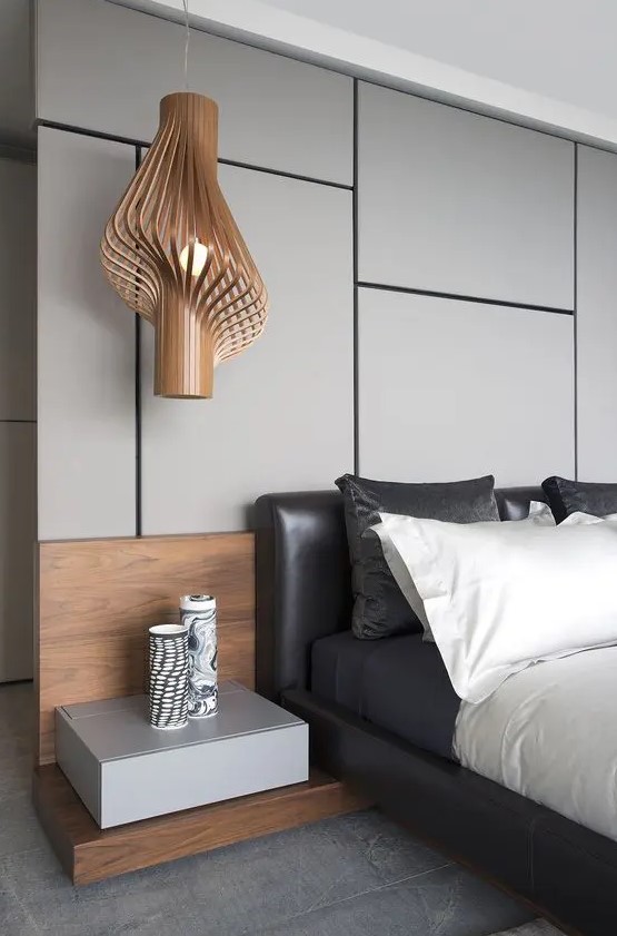 a gorgeous contemporary bedroom with a grey panel accent wall, a black leather bed, contrasting bedding, a floating nightstand and a jaw dropping pendant lamp