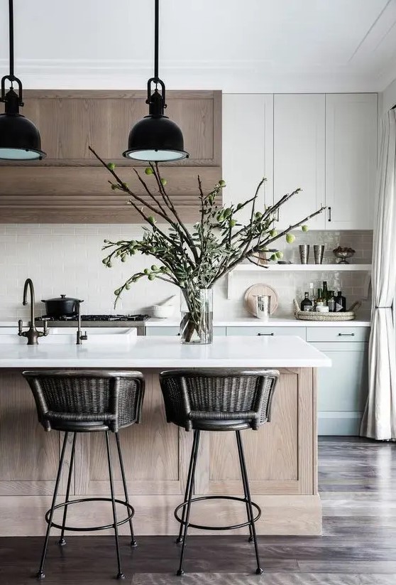 a gorgeous contemporary kitchen with white, dove grey shaker cabients, a stained hood, a stained kitchen islannd, black pendant lamps and woven stools