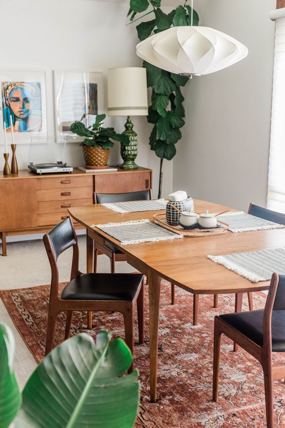 a gorgeous mid-century modern dining room with a stained credenza, a table and black leather chairs, potted greenery and a printed rug