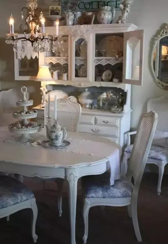 a gorgeous vintage dining room with shabby chic furniture, an elegant buffet, a crystal chandelier and chic porcelain