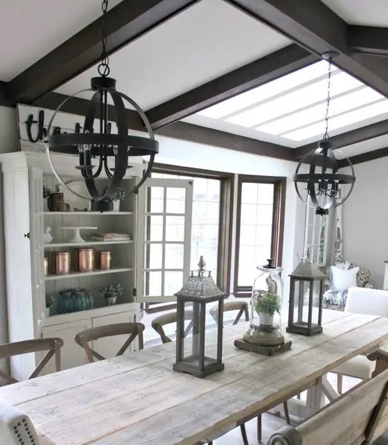 a greige farmhouse dining room with dark stained wooden beams, a whitewashed wooden dining set, an elegant buffet and sphere chandeliers