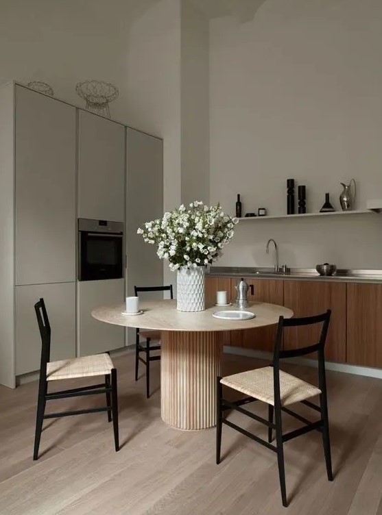 a greige kitchen combined with a kitchen, light stained furniture, a round table and woven chairs, a grey storage unit, a long shelf and some blooms