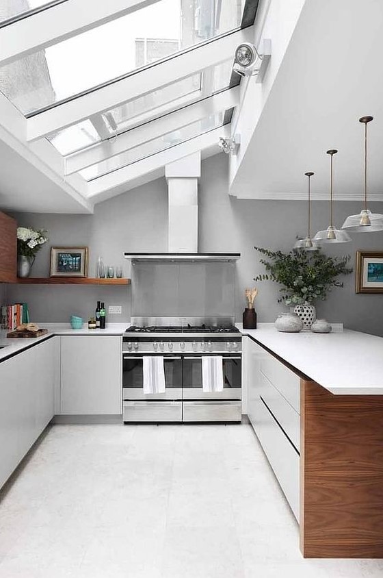 a large neutral attic kitchen with a glazed ceiling, sleek white cabinets and countertops, pendant lamps and grey walls