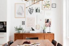 a light-filled mid-century modern dining nook with a stained credenza and table, black chairs, a classic chandelier and a gallery wall