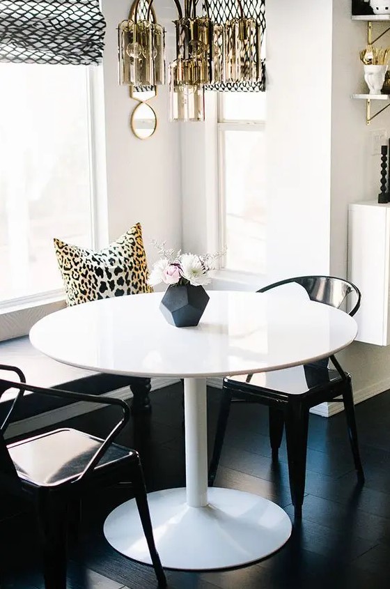 a little glam dining space with a built-in bench, a round table, black chairs, a gilded chandelier, printed elements
