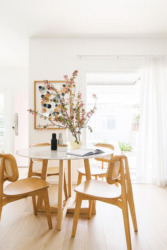 a lively Scandinavian dining space with a round table and stained chairs, a bright artwork and lots of natural light